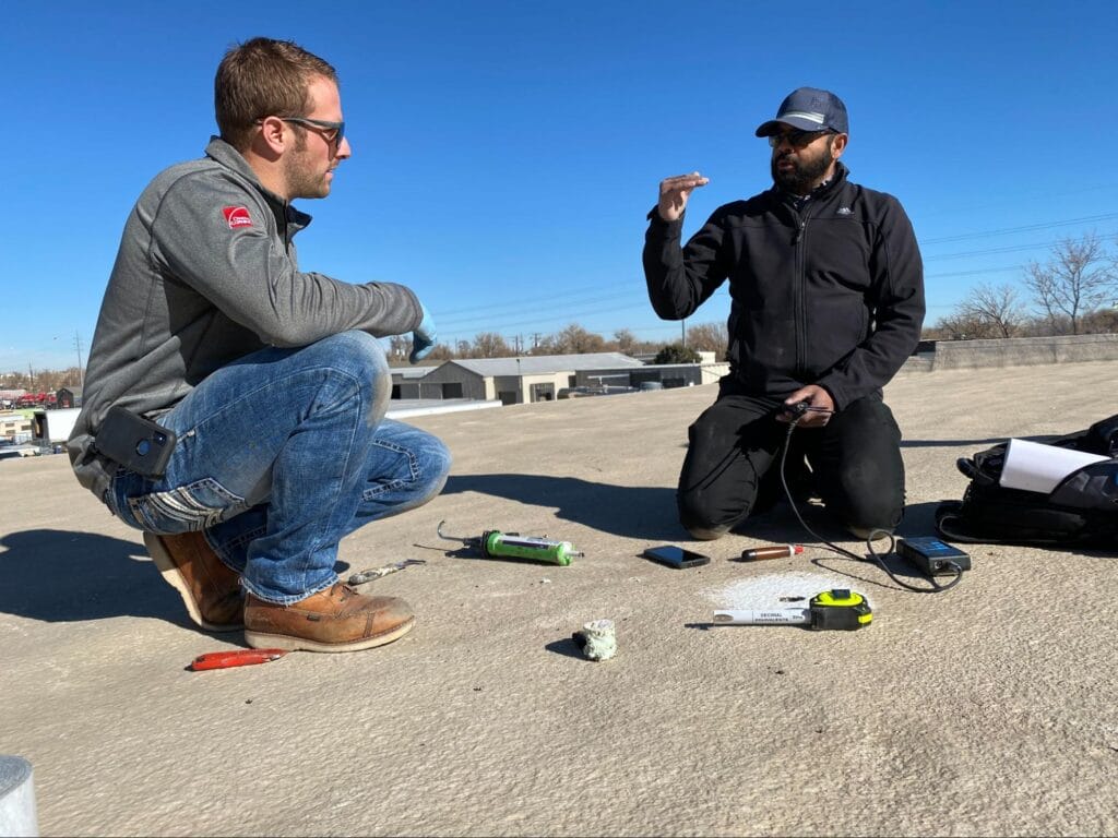 Two professionals inspecting a commercial roof system and discussing repairs. 
