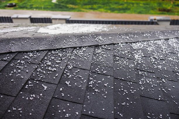 Hail damage visible on asphalt roof shingles after a storm.