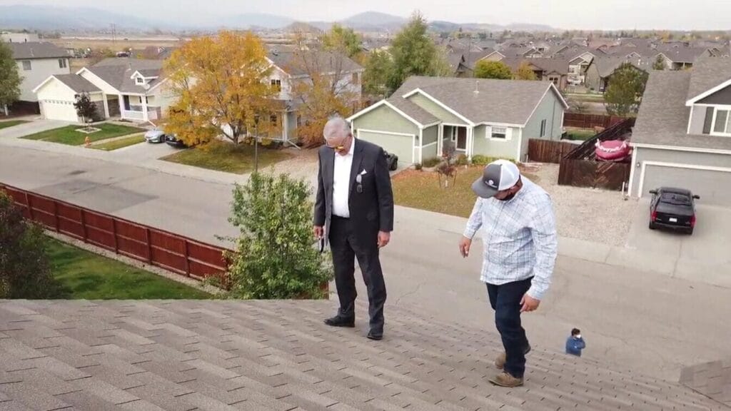 Roofing contractor and homeowner inspect architectural asphalt shingles on a residential roof.